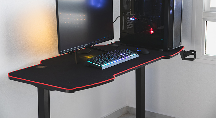 Ein schwarzer Schreibtisch mit roter Umrandung steht vor einer Wand. Auf dem Tisch stehen ein Monitor, eine Tastatur und ein PC-Gehäuse.