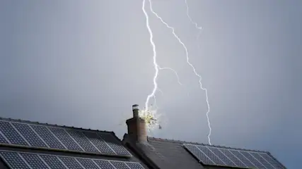 Blitz schlägt in einen Schornstein eines Hauses mit Solarpanels auf dem Dach ein.