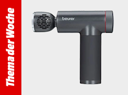 Dunkelgraue Massagepistole in T-Form mit vertikalem Griff und rotem Akzentring am Kopf; links ein roter, vertikaler Balken mit weißer Schrift „Thema der Woche“.