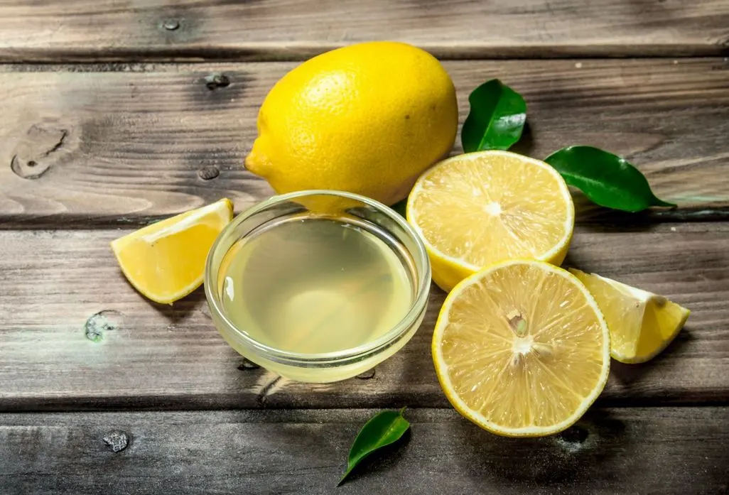 Zitronensaft in einer kleinen Schuessel mit frischen Zitronen