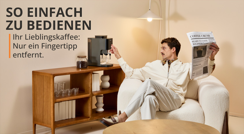 Mann sitzt auf Sessel, bedient Krups Kaffeemaschine, liest Zeitung. SO EINFACH ZU BEDIENEN: Lieblingskaffee nur ein Fingertipp entfernt.