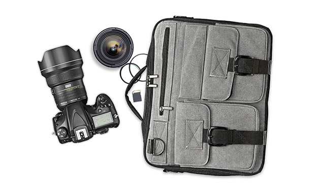 Eine schwarze Kamera und Objektive liegen neben einer grauen Kameratasche mit mehreren Fächern und schwarzen Schnallen.