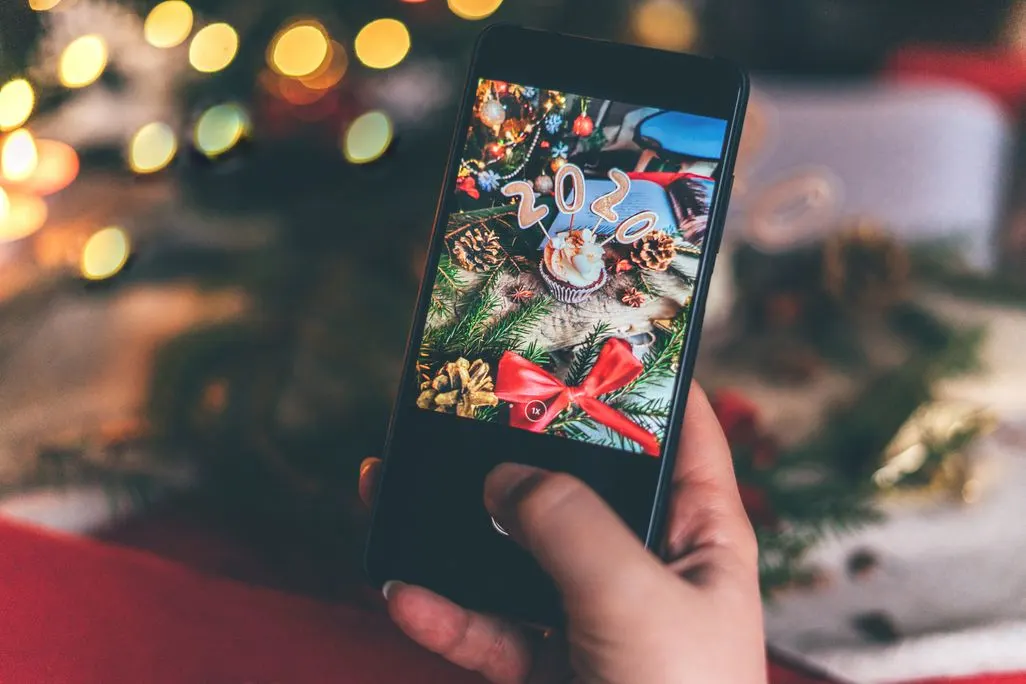 Hand haelt ein Smartphone und fotografiert Weihnachtsdeko mit der Zahl 2020.