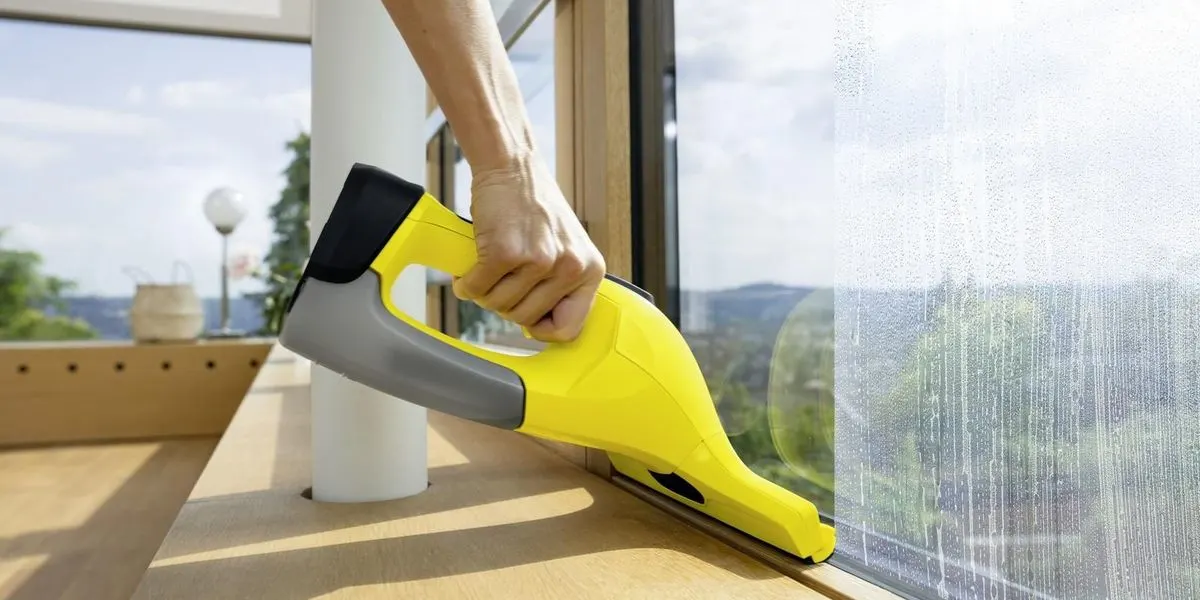 Hand reinigt ein Fenster mit einem gelben Akku Fenstersauger