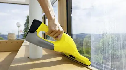 Hand reinigt ein Fenster mit einem gelben Akku Fenstersauger