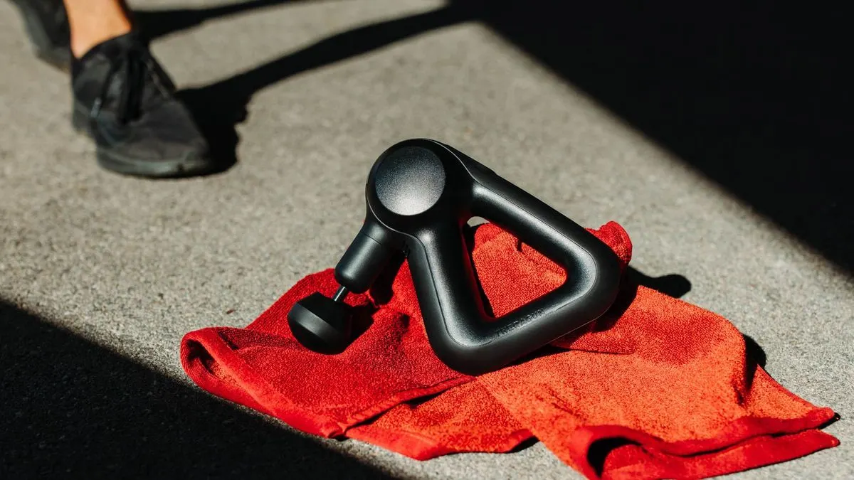 Schwarze Massagepistole liegt auf einem roten Handtuch auf dem Boden