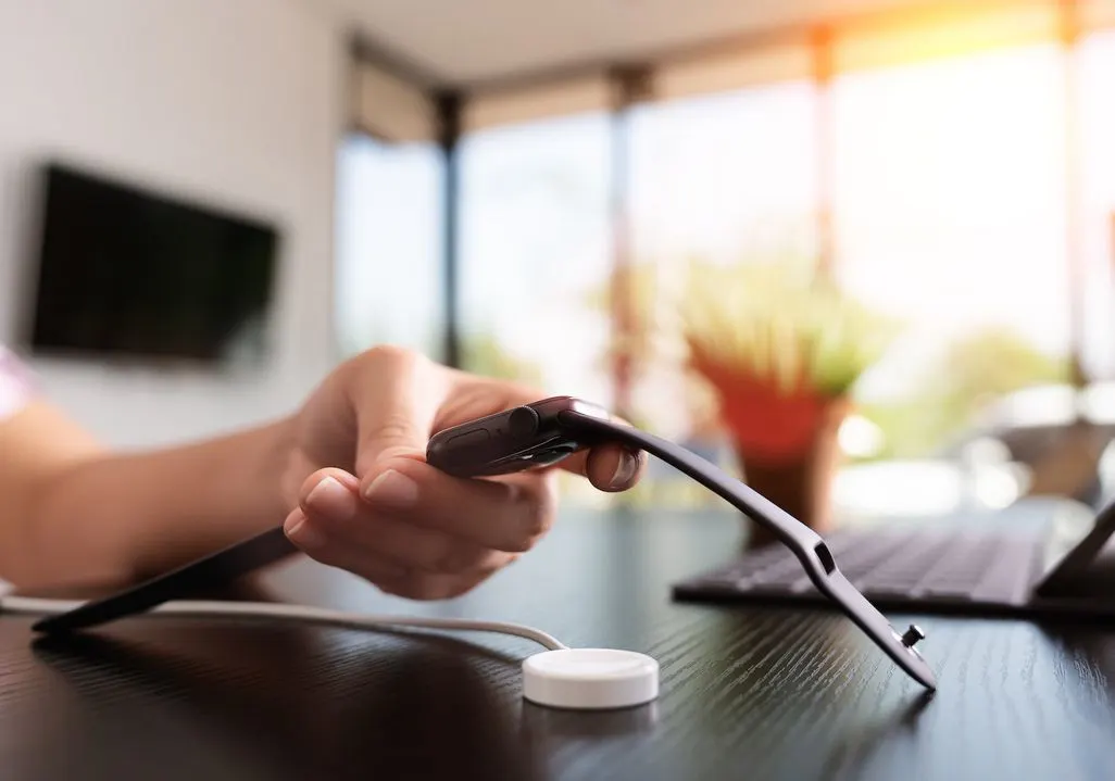 Hand legt eine Smartwatch auf eine magnetische Ladestation auf einem Schreibtisch.