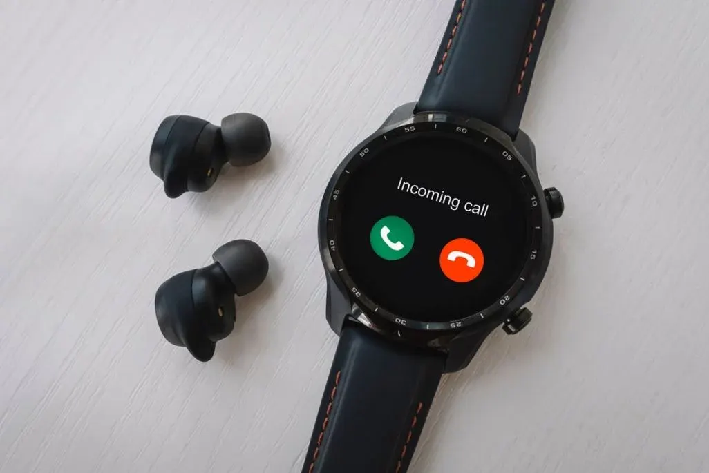 Smartwatch zeigt Incoming Call am Display, Headbuds liegen daneben.