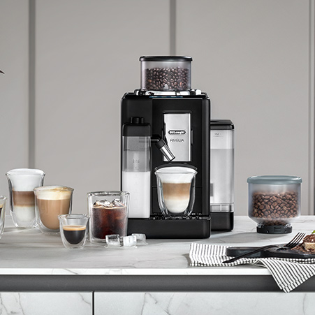 Eine Kaffeemaschine mit Kaffeebohnen steht auf einer Theke. Es gibt verschiedene Getränke, darunter Kaffee und Milch.