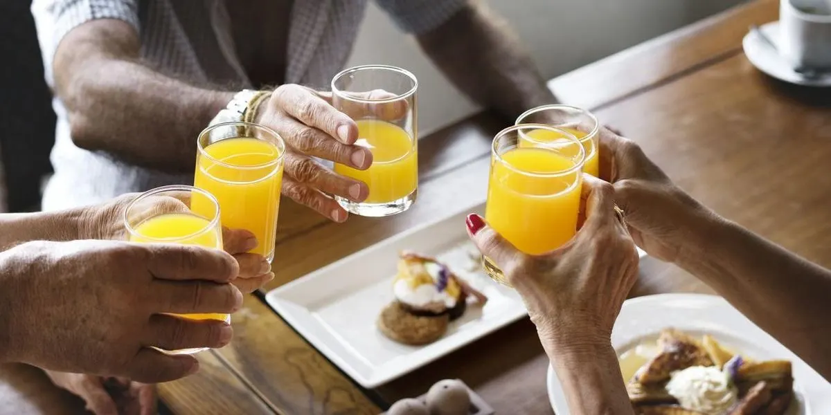 Mehrere Personen stossen mit Glaesern voller Orangensaft beim Fruehstueck an
