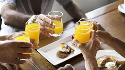 Mehrere Personen stossen mit Glaesern voller Orangensaft beim Fruehstueck an