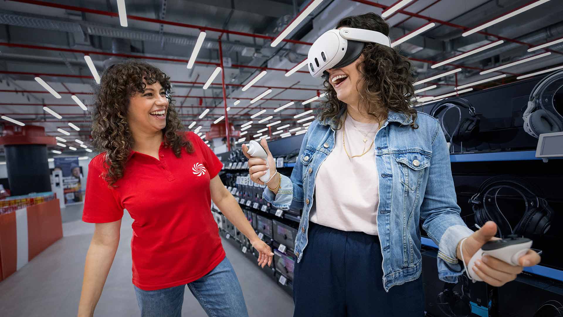 Ein Paar sitzt auf einem grauen Sofa und hält Videospiel-Controller in den Händen. Neonbeleuchtung an der Decke.