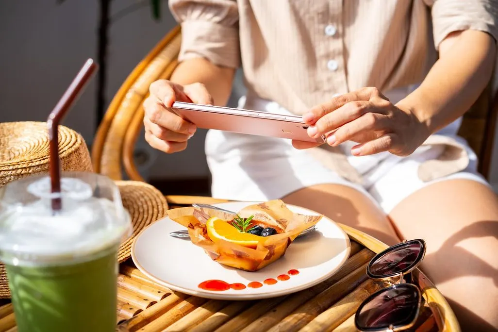 Person fotografiert Dessert mit Smartphone auf einem Tisch im Freien.