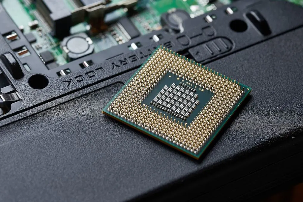 Ein grüner Computer-Chip mit goldenen Pins und einer grauen Oberfläche liegt auf einer dunklen Fläche.