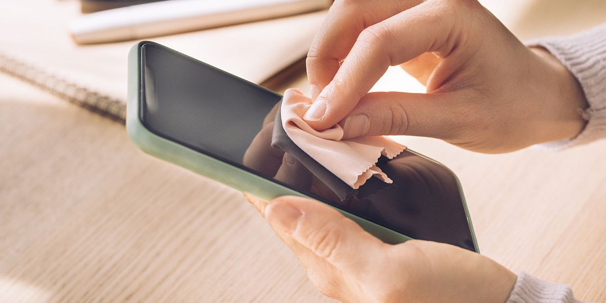 Haende reinigen die Oberflaeche eines Smartphones mit einem Mikrofasertuch