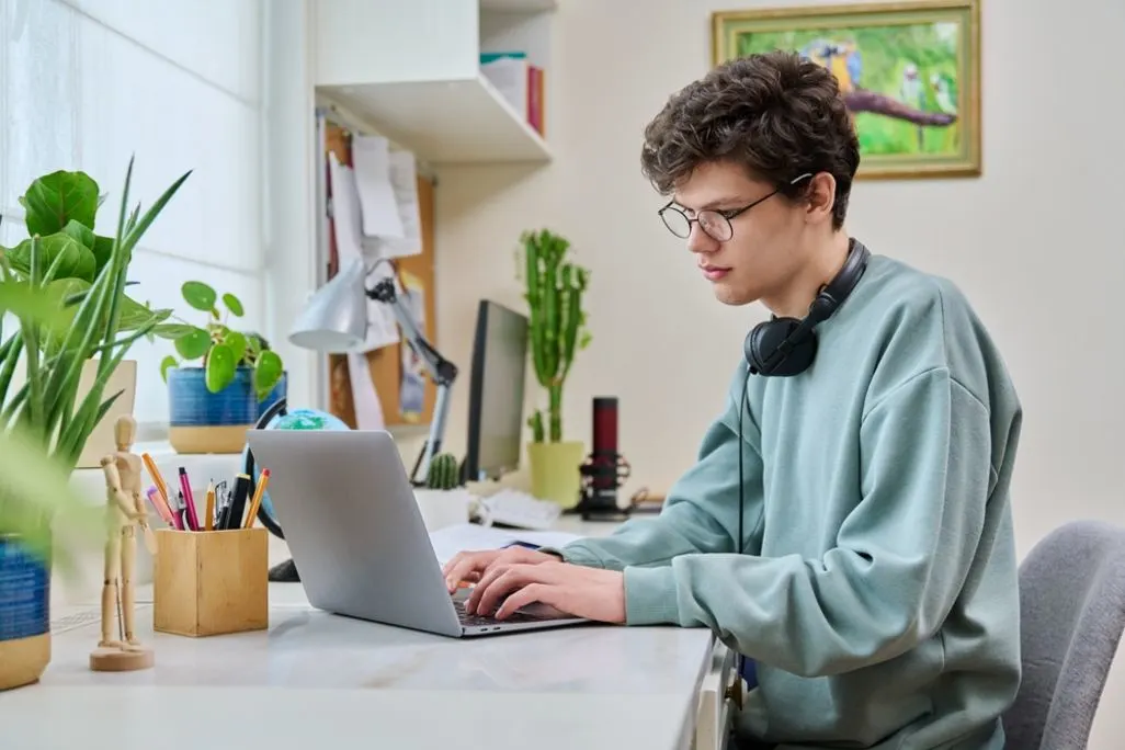 Junger Mann mit Brille tippt konzentriert am Laptop an seinem Schreibtisch