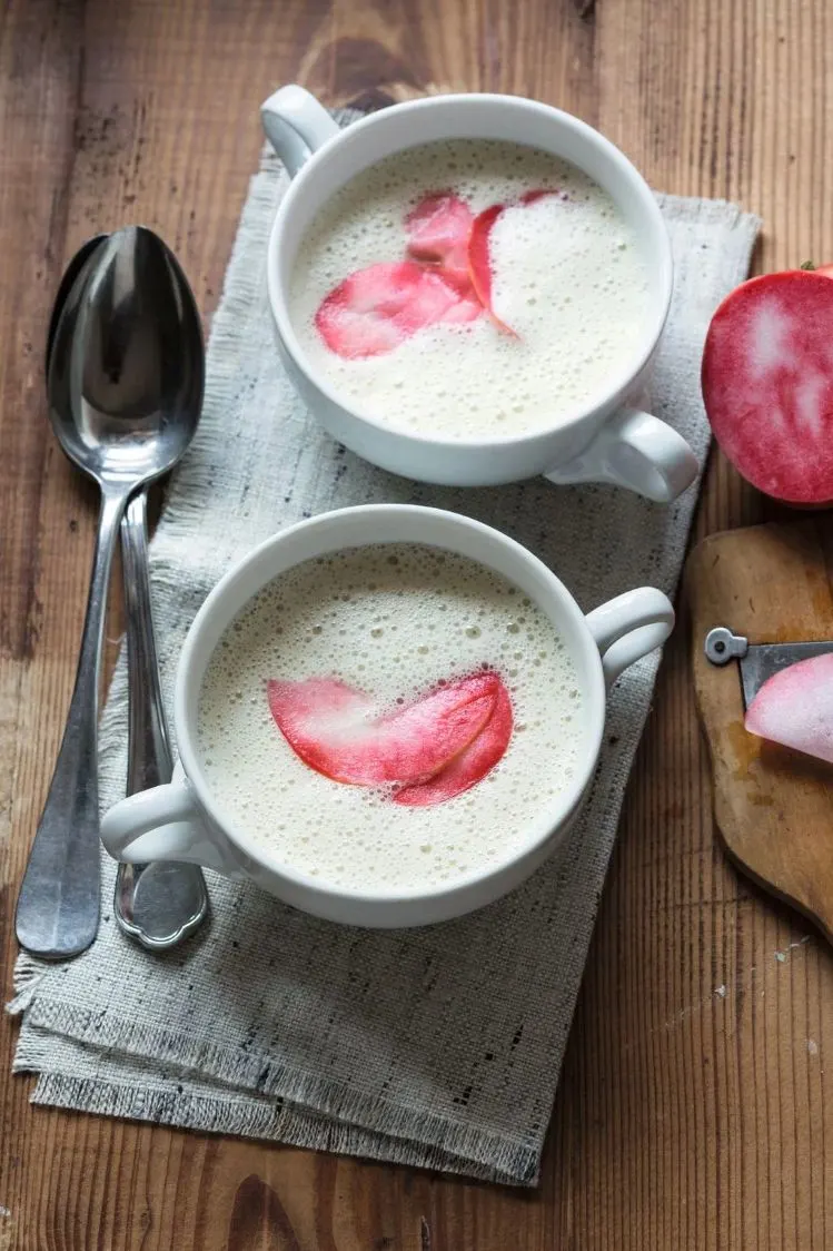 Zwei Schalen mit Apfel-Sellerie Suppe garniert mit einer hauchdünnen roten Apfelscheibe.
