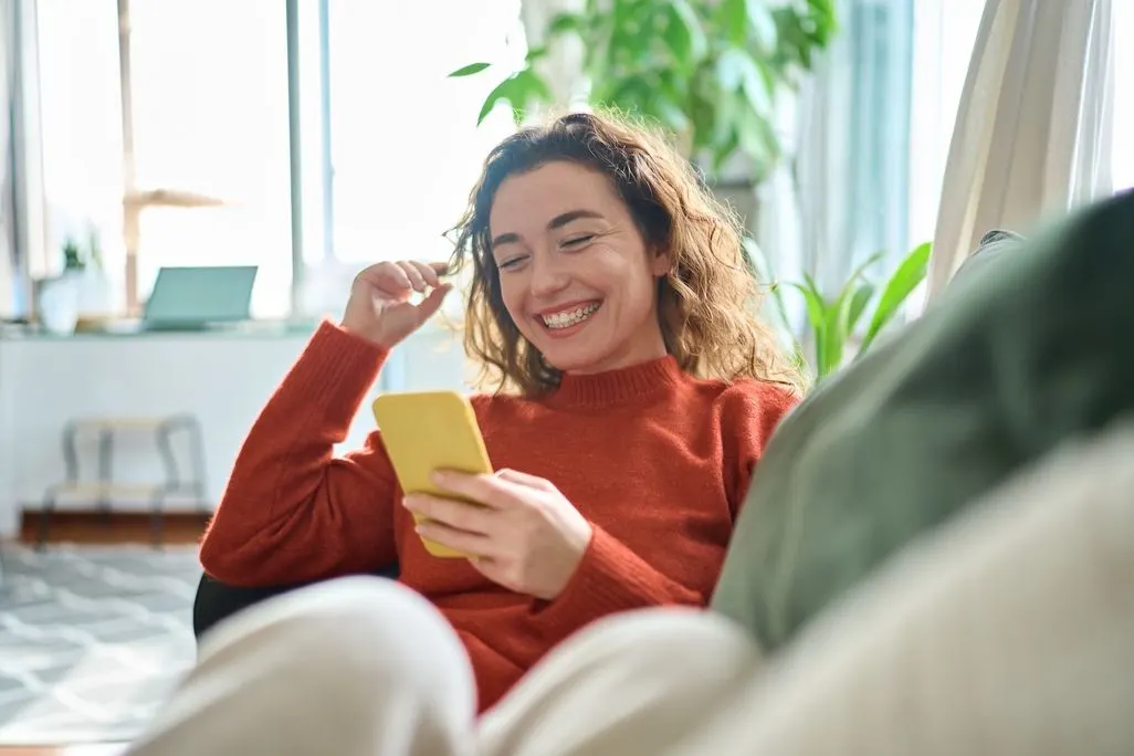 Eine Person mit lockigem Haar sitzt auf einem Sofa und nutzt ein gelbes Smartphone