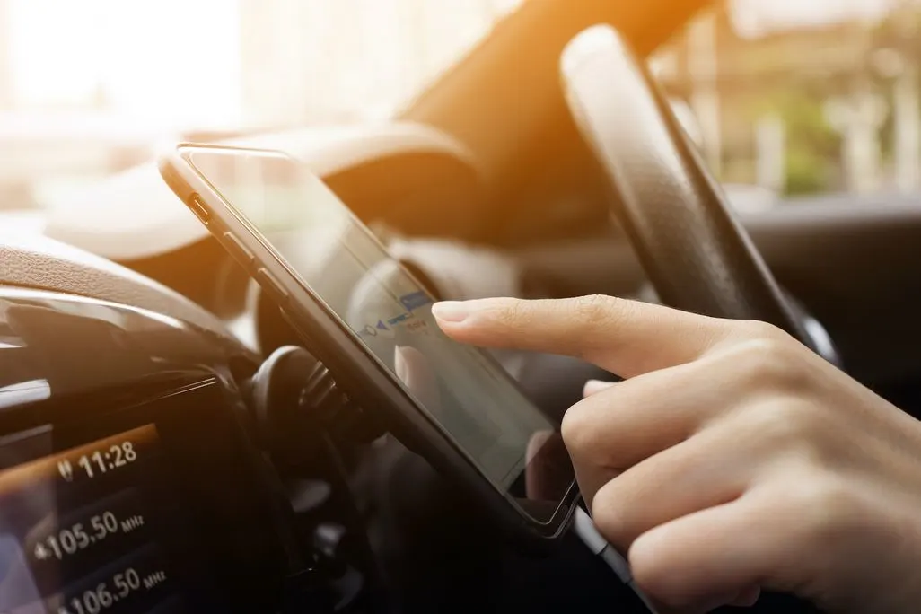 Eine Hand bedient ein Smartphone mit Navigationsapp an einer Halterung im Auto