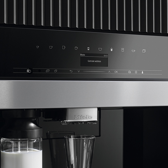 Nahaufnahme eines schwarzen Kaffeevollautomaten mit Milchbehälter und Glas.