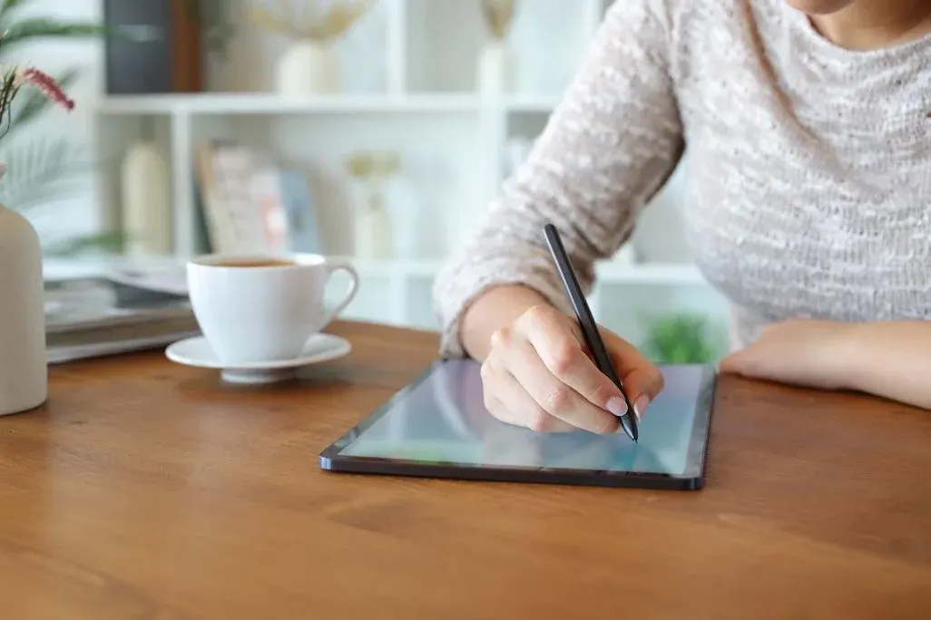 Frau schreibt am Tisch auf einem Tablet mit einem Eingabestift.
