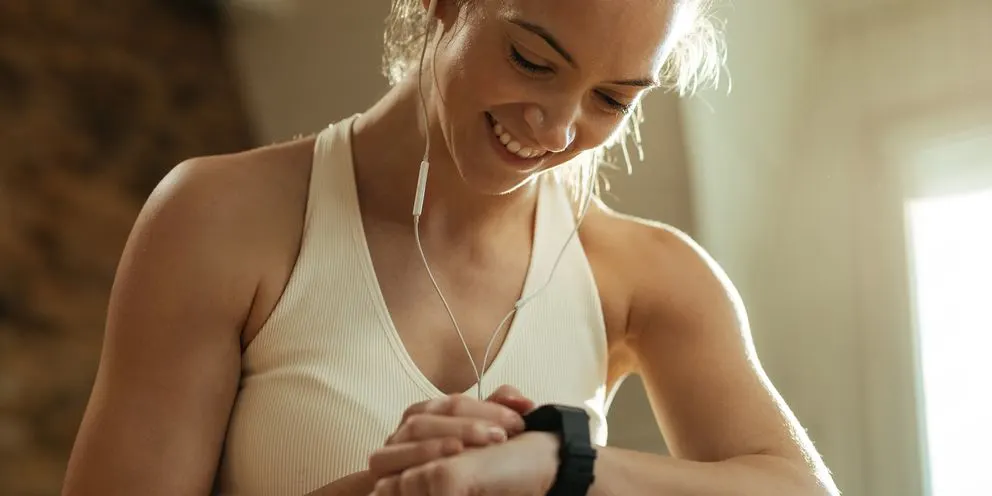 Frau in Sportkleidung schaut auf ihre Smartwatch waehrend sie Kopfhoerer traegt