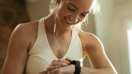 Frau in Sportkleidung schaut auf ihre Smartwatch waehrend sie Kopfhoerer traegt