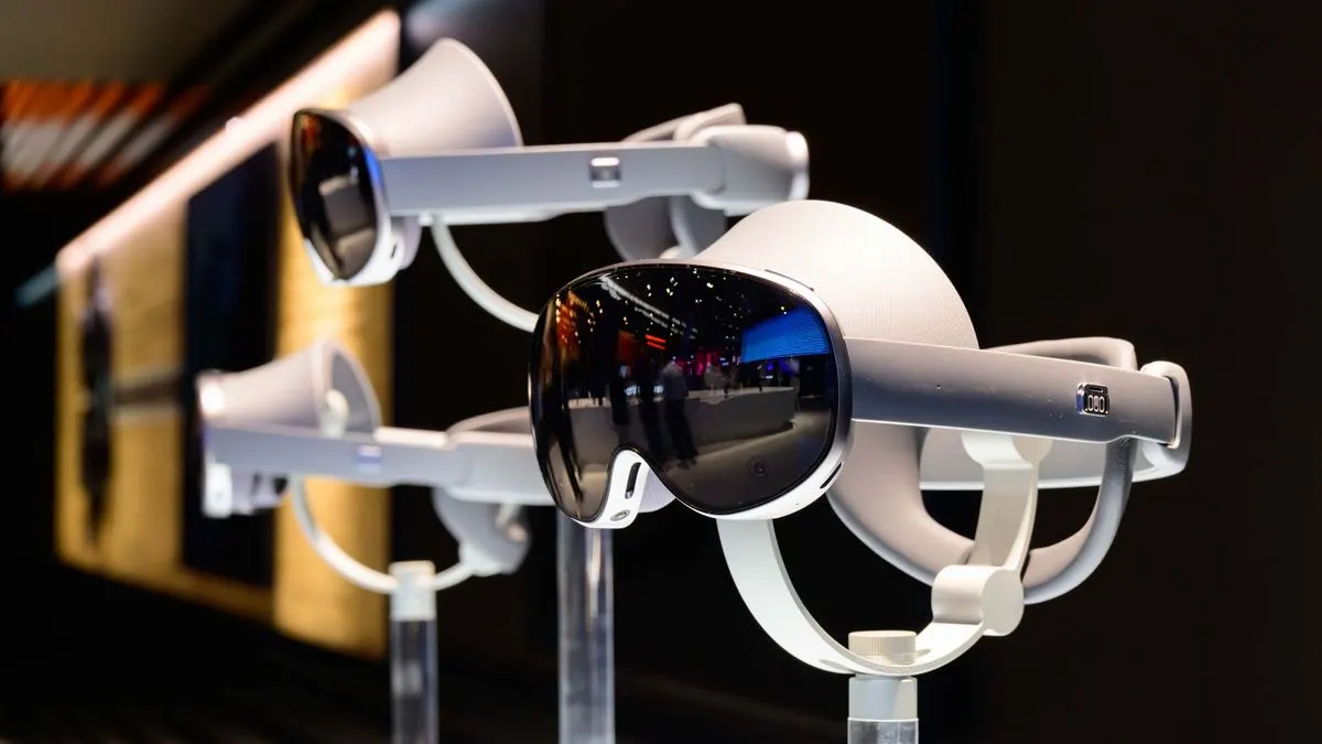 Zwei hellgraue VR-Headsets auf Ständern. Das vordere hat ein dunkles, spiegelndes Visier mit Reflexionen einer Ausstellung.