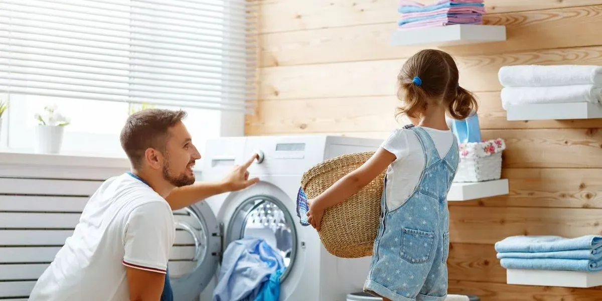 Mann stellt eine Waschmaschine ein und ein Kind bringt einen Korb
