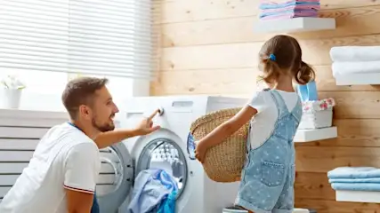 Mann stellt eine Waschmaschine ein und ein Kind bringt einen Korb
