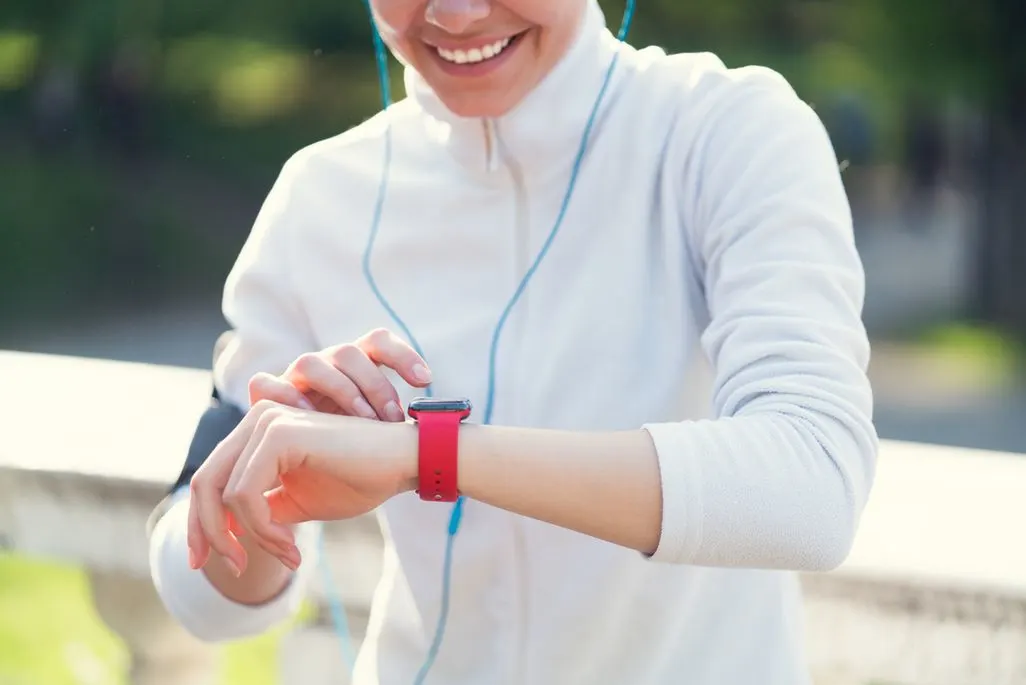 Frau in weißem Pullover bedient eine Smartwatch mit rotem Armband und lächelt.