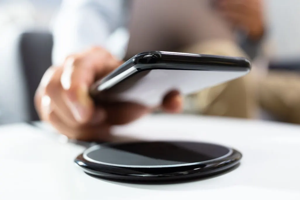 Hand legt ein Smartphone auf eine schwarze kabellose Ladestation