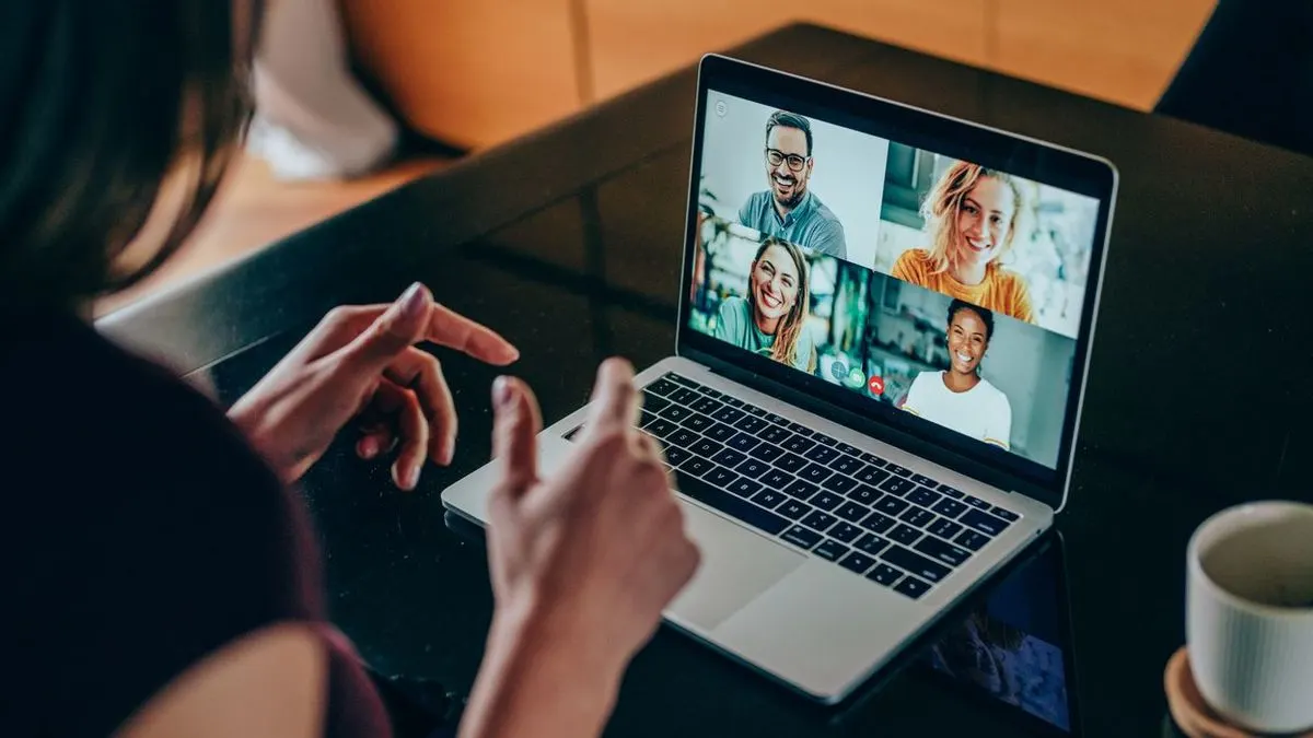 Person sitzt an einem Tisch und nimmt an einer Videokonferenz mit vier Teilnehmern am Laptop teil. Auf dem Tisch steht eine Tasse.