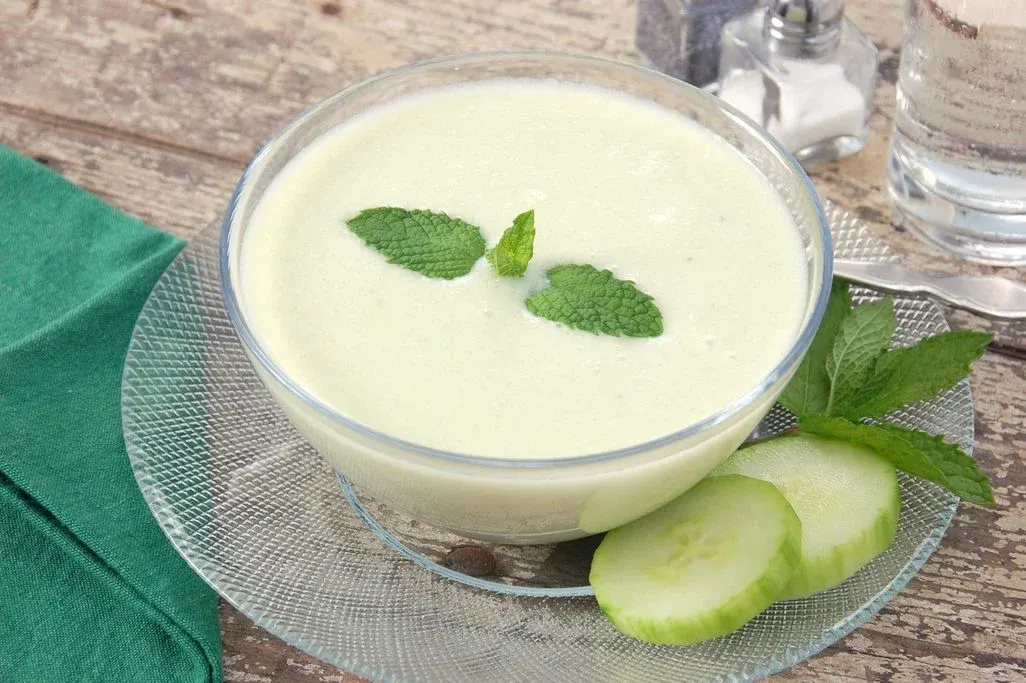 Grüne Sommersuppe in Glasschale mit Minze und Gurkenscheiben dekoriert.
