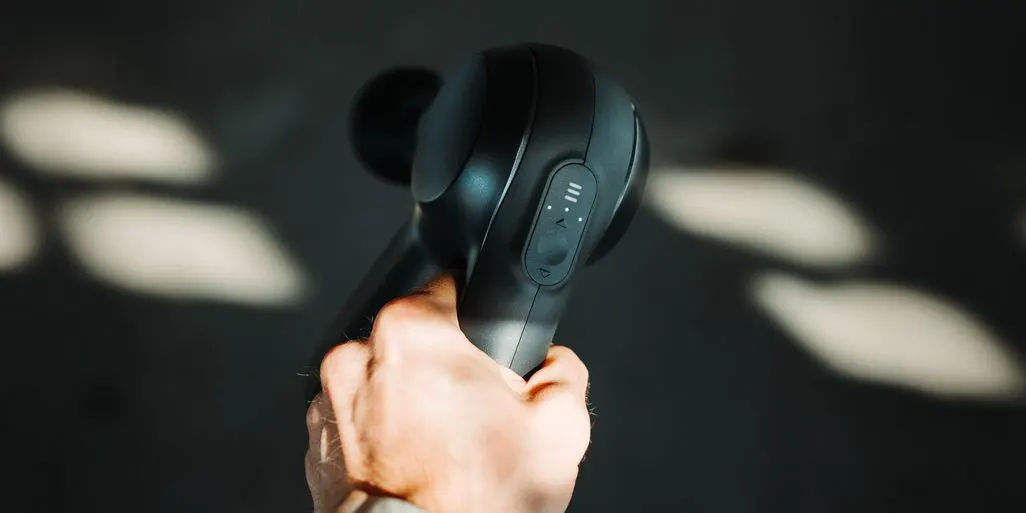 Nahaufnahme einer Hand, die eine schwarze Massagepistole mit Bedienfeld festhält.