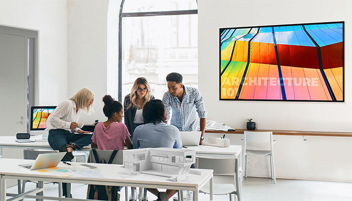In einem hellen Büro stehen Tische mit Computern und einem Architekturmodell. Ein farbenfrohes Bild hängt an der Wand.