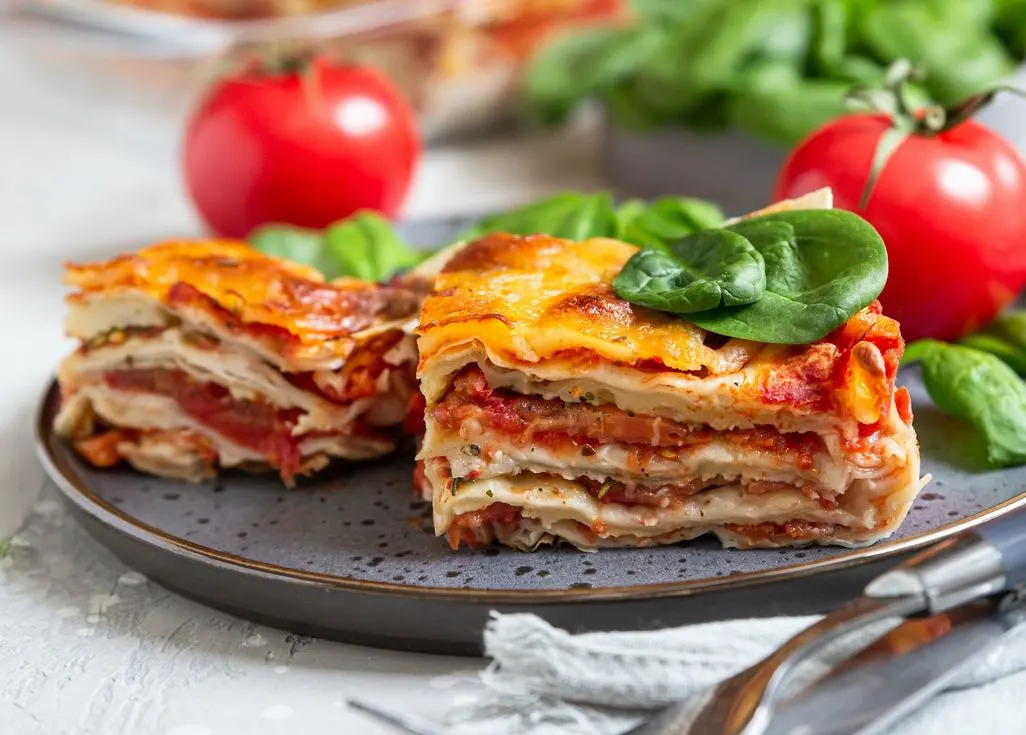 Zwei Stücke vegetarische Lasagne mit Spinatblättern auf einem Teller.