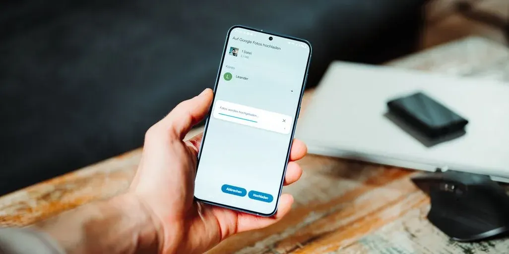 Handy zeigt Cloud-Speicher-App, Hand hält das Smartphone über einem Tisch.
