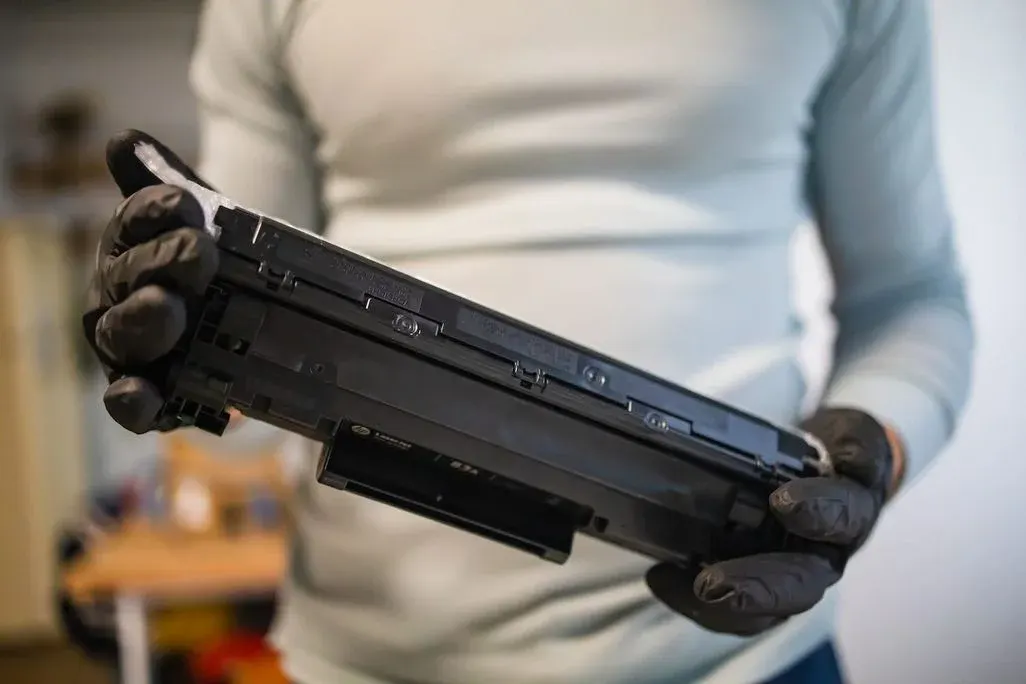 Person mit schwarzen Handschuhen hält eine schwarze Tonerkartusche für Laserdrucker, Nahaufnahme.