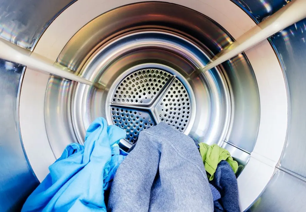 Blick in die geöffnete Trommel eines Wäschetrockners mit bunter Kleidung