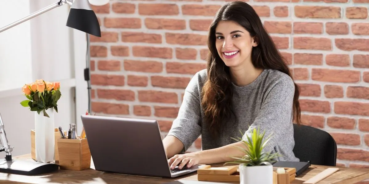 Lächelnde Frau arbeitet am Laptop in modernem Buero mit Backsteinwand