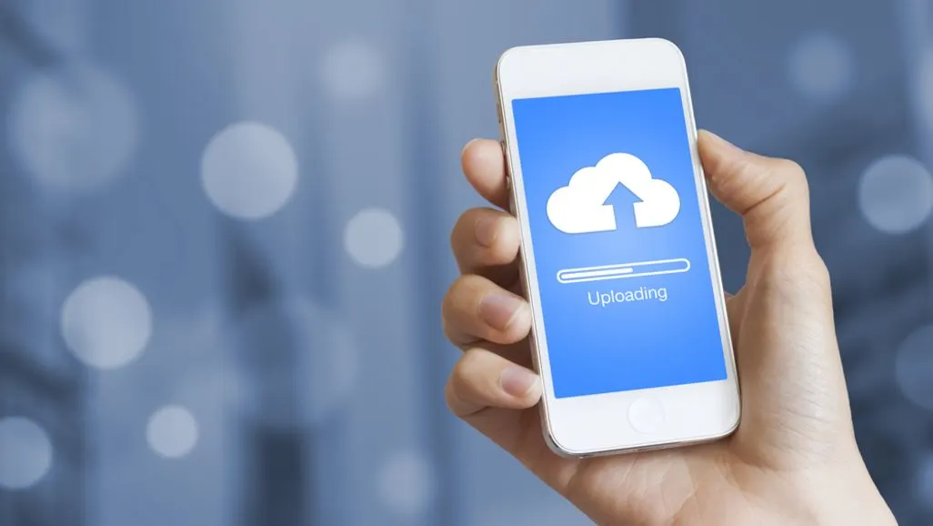 Hand hält Smartphone mit Cloud Upload Symbol auf dem Bildschirm.