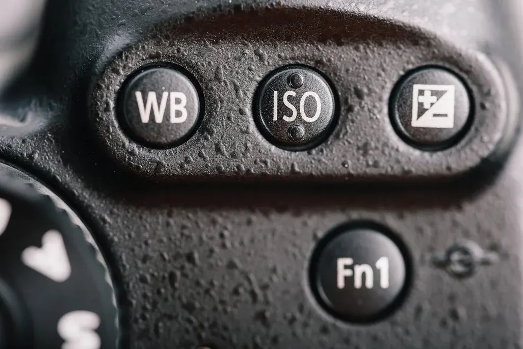 Nahaufnahme einer schwarzen Digitalkamera mit Wassertropfen. Sichtbar sind Tasten für WB, ISO, Belichtungskorrektur und Fn1.