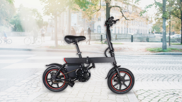 Schwarzes E-Bike mit rotem Akzent auf Pflastersteinen. Im Hintergrund Bäume und Gebäude bei Tageslicht.