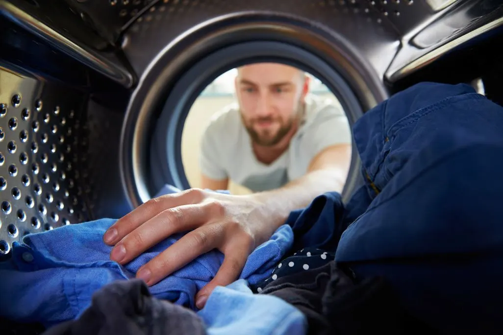Blick aus dem Inneren einer Waschmaschine auf eine Person, die Wäsche einlegt