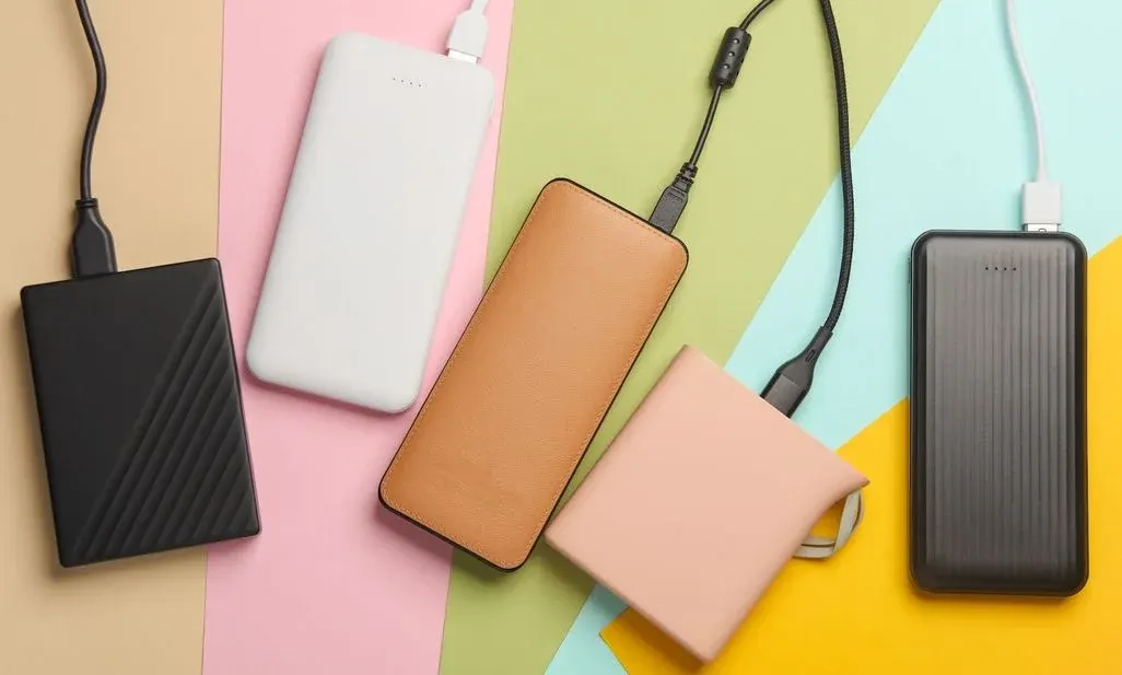 Verschiedene externe Festplatten und Power Banks in unterschiedlichen Farben und Designs auf buntem, farbigem Hintergrund
