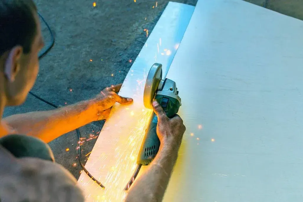 Handwerker bearbeitet Stahlblech mit gelb-schwarzem Elektroschleifers, intensive Funkenspritzer beim Schleifen sichtbar