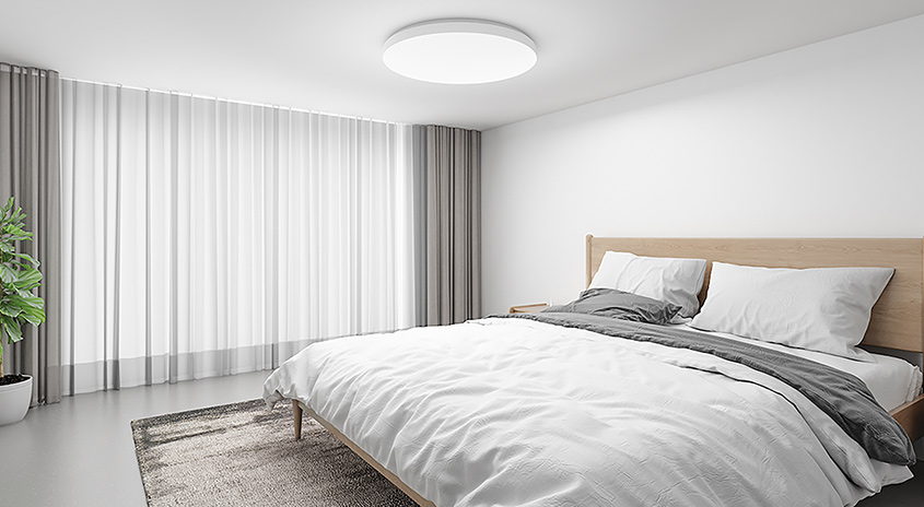 Ein helles Schlafzimmer mit einem Bett, Vorhängen und einer Zimmerpflanze.