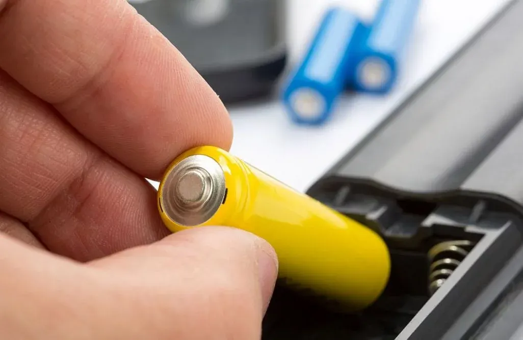Nahaufnahme einer Hand die eine Batterie in die Fernbedienung gibt