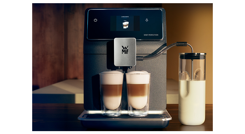 Kaffeevollautomat mit zwei Latte Macchiato Gläsern und Milchbehälter auf einer dunklen Oberfläche vor braunem Hintergrund.